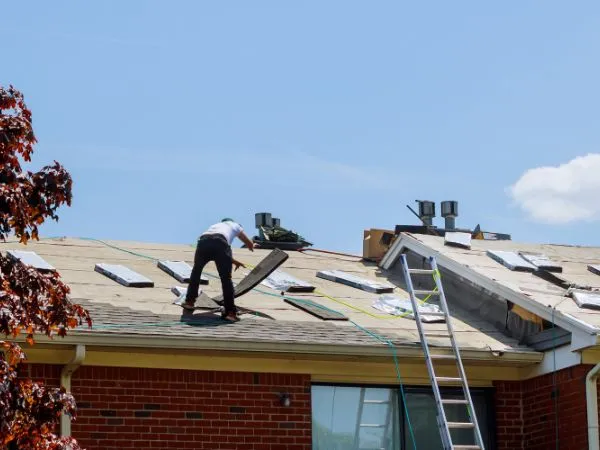 Roofer removing damaged asphalt shingles from a brick home roof