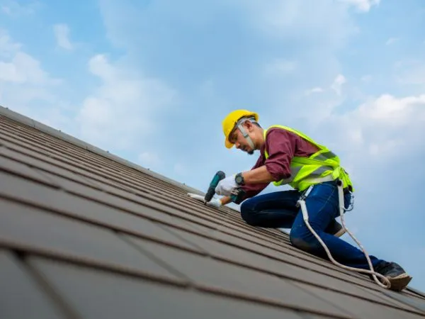 Roofer in a safety harness installing shingles on a roof
