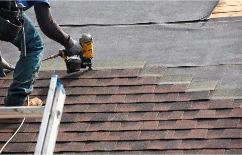 Roofer using a nail gun to install asphalt shingles